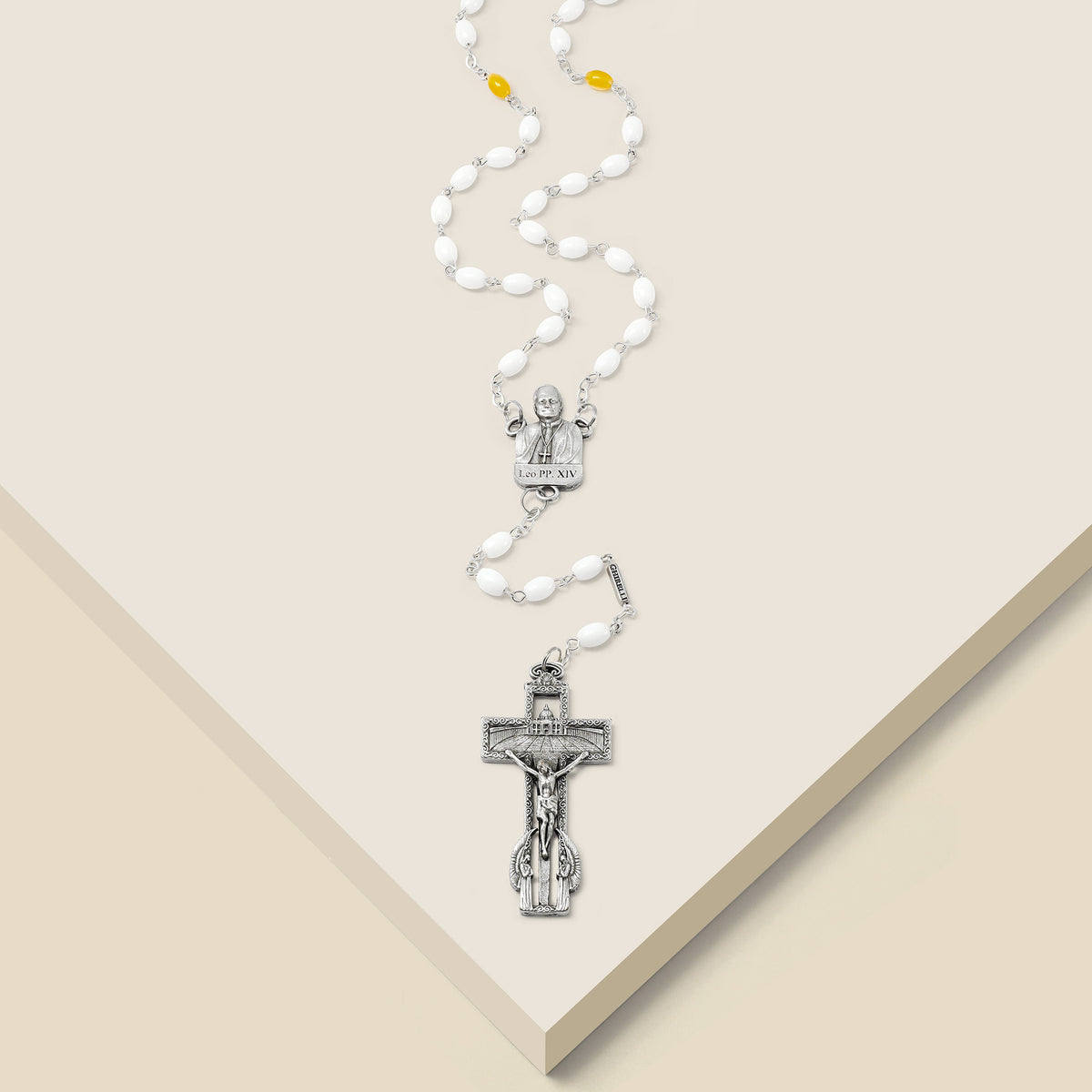 Rosary with white beads and silver crucifix on a beige background
