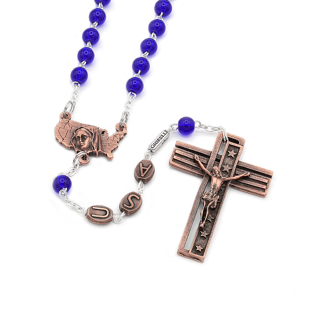 A rosary with antique copper finish and cobalt blue glass beads, featuring a crucifix with an inscription and a centerpiece with an image of the Immaculate Conception and a map of the U.S.