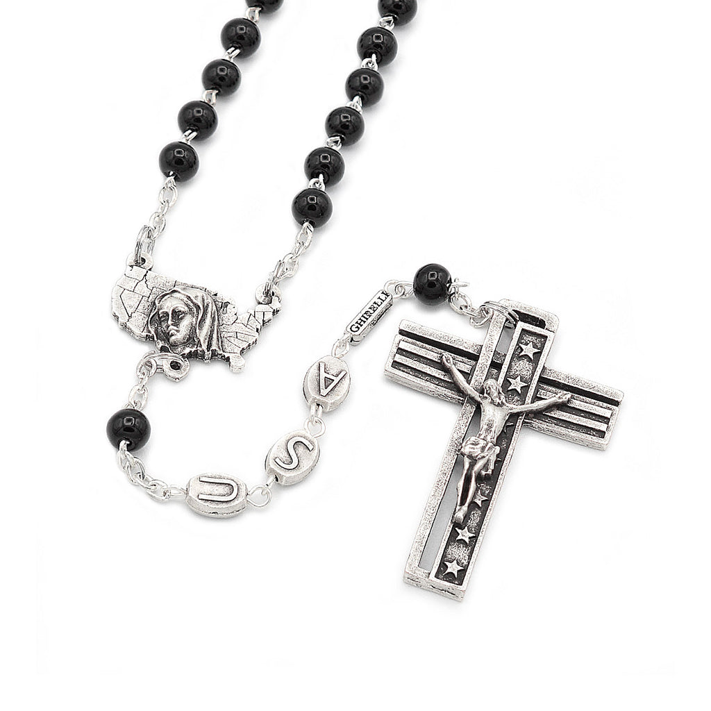 A silver rosary with black glass beads, featuring a crucifix with an inscription and a centerpiece with an image of the Immaculate Conception.