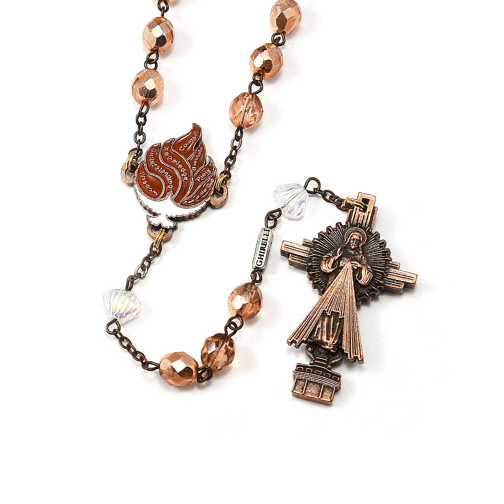 A close-up image of a rosary with bronze-colored beads and a detailed metal crucifix featuring an artistic representation of the Merciful Jesus and the Eucharistic Host.