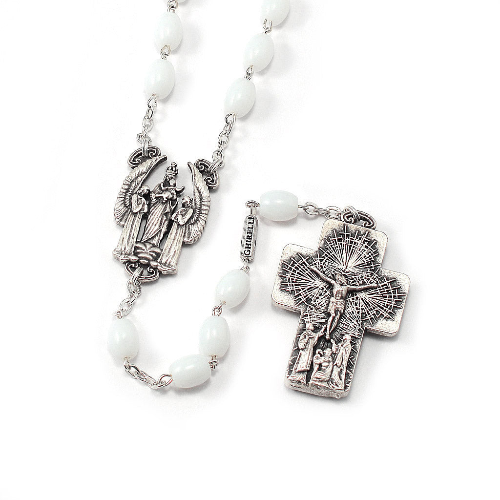 A silver-colored metal rosary with white oval glass beads, featuring a cross on one end and a depiction of Christ and the Virgin Mary on the other.