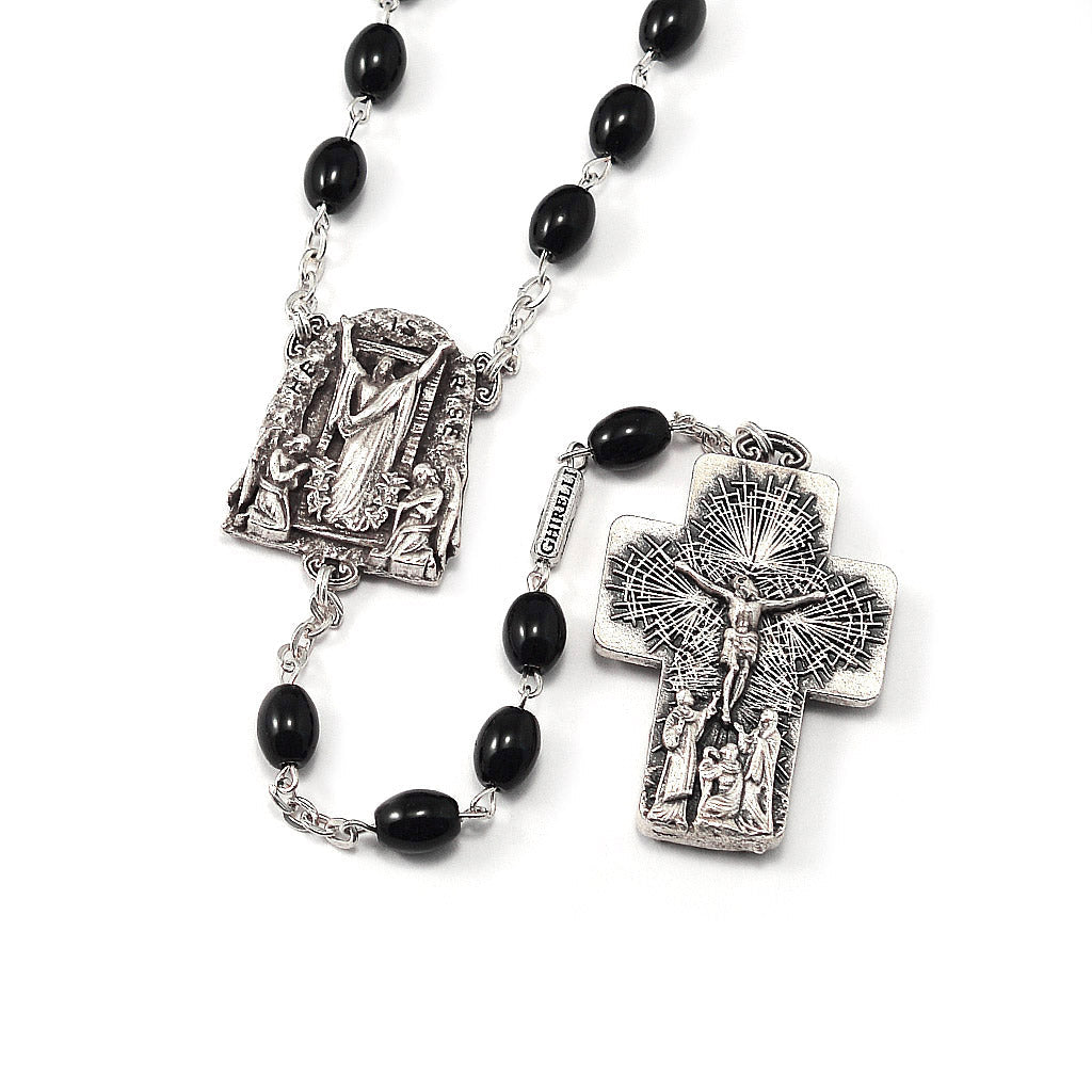 A rosary with black oval glass beads and silver metallic components, including a crucifix and a detailed centerpiece depicting &#39;The Resurrection of Christ&#39;.