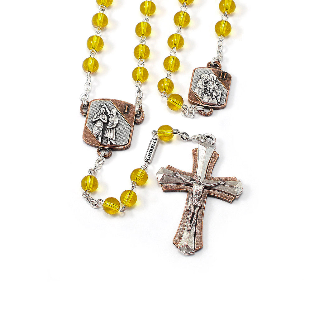 A yellow beaded rosary with two-tone (antique silver and antique copper) crucifix and medals, including a detailed image of Jesus and text on the reverse.