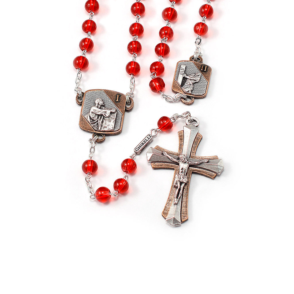 A red bead rosary with detailed medals depicting scenes from the Sorrowful Mysteries of the Rosary, featuring a two-tone silver and copper crucifix.