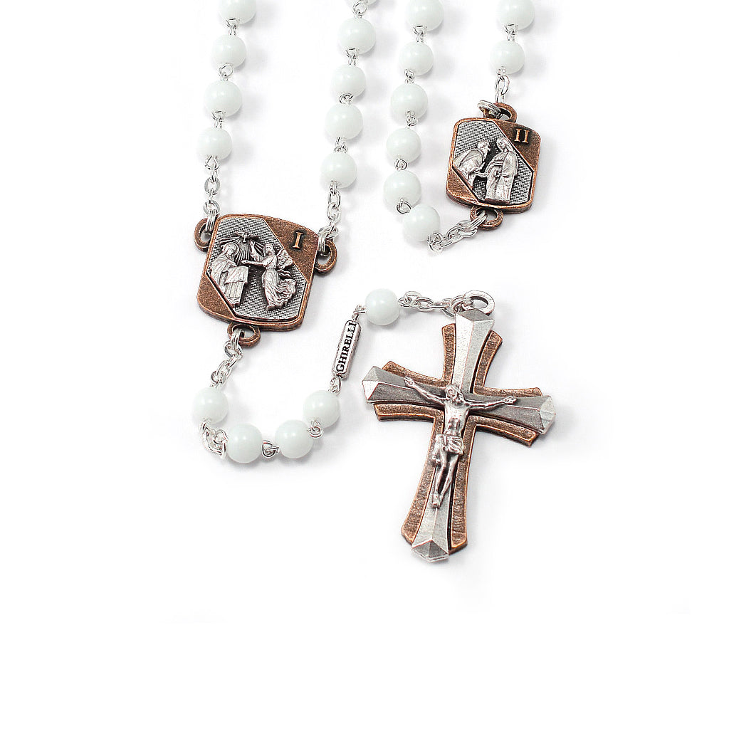 A white beaded rosary with antique silver and antique copper colored medals, including a two-tone crucifix and a detailed center medal.