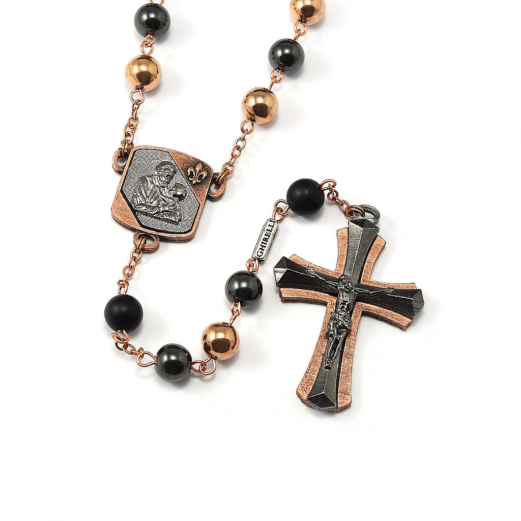 A rosary with black hematite beads, gunmetal and copper polish finish, featuring a crucifix and a centerpiece with a depiction of Saint Joseph.